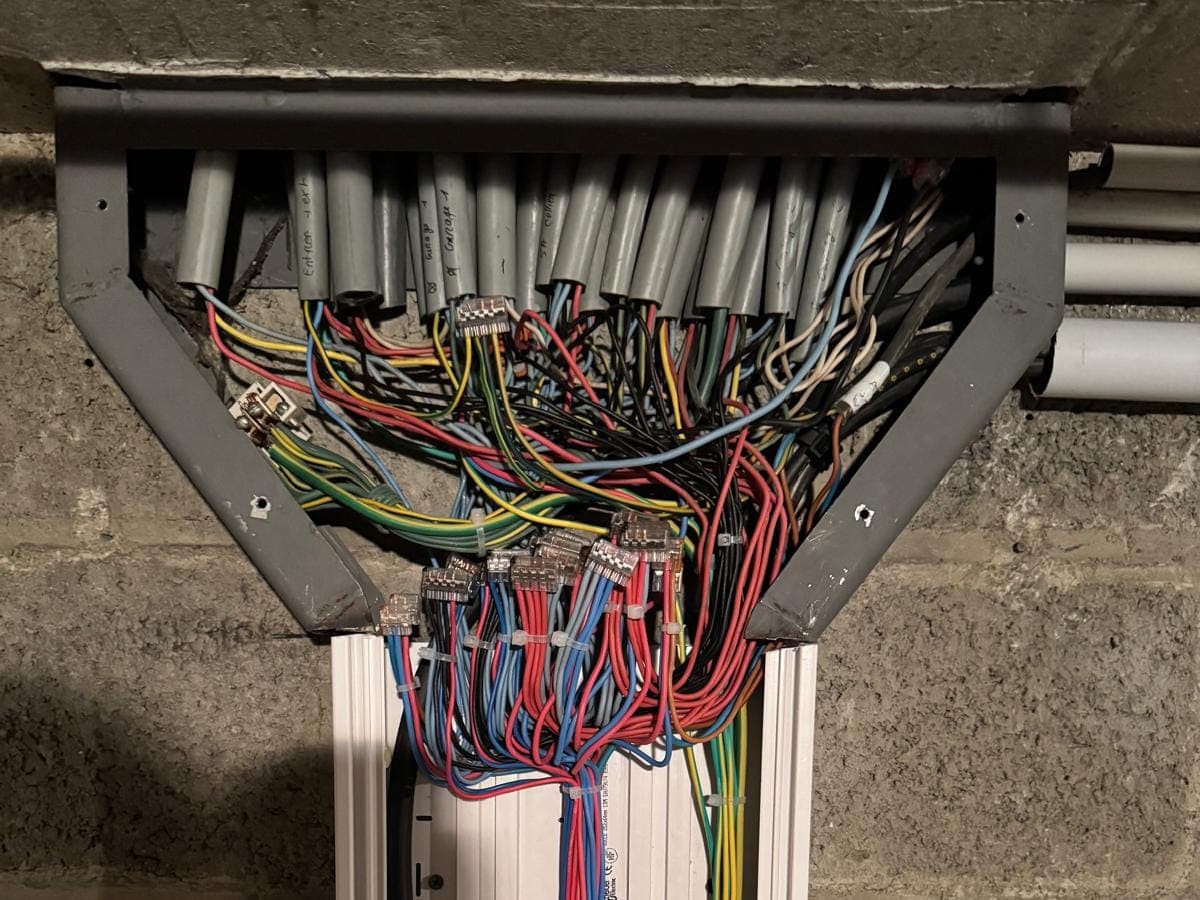 Conduits regroupés dans un chemin de câbles, conducteurs repérés par couleur descendant vers une goulotte.